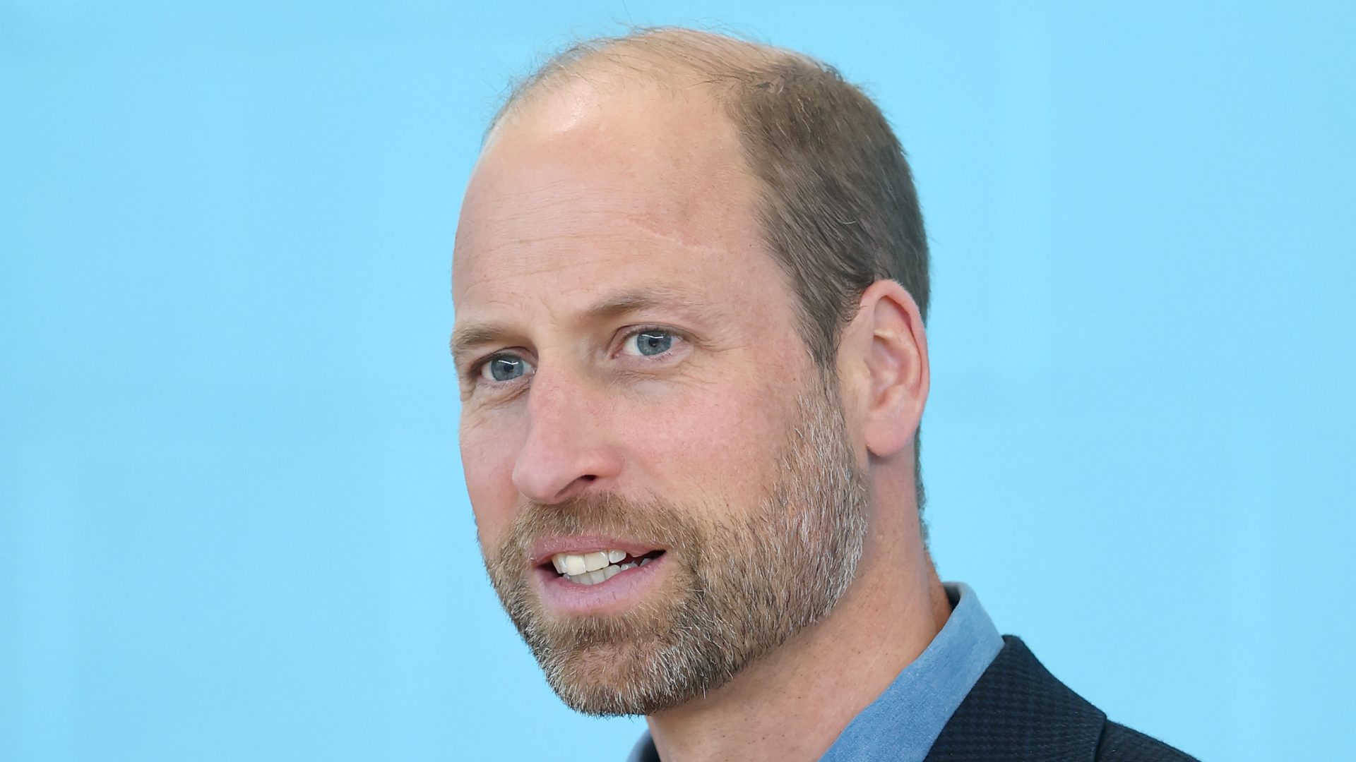 A headshot of Prince William smiling in a blue shirt