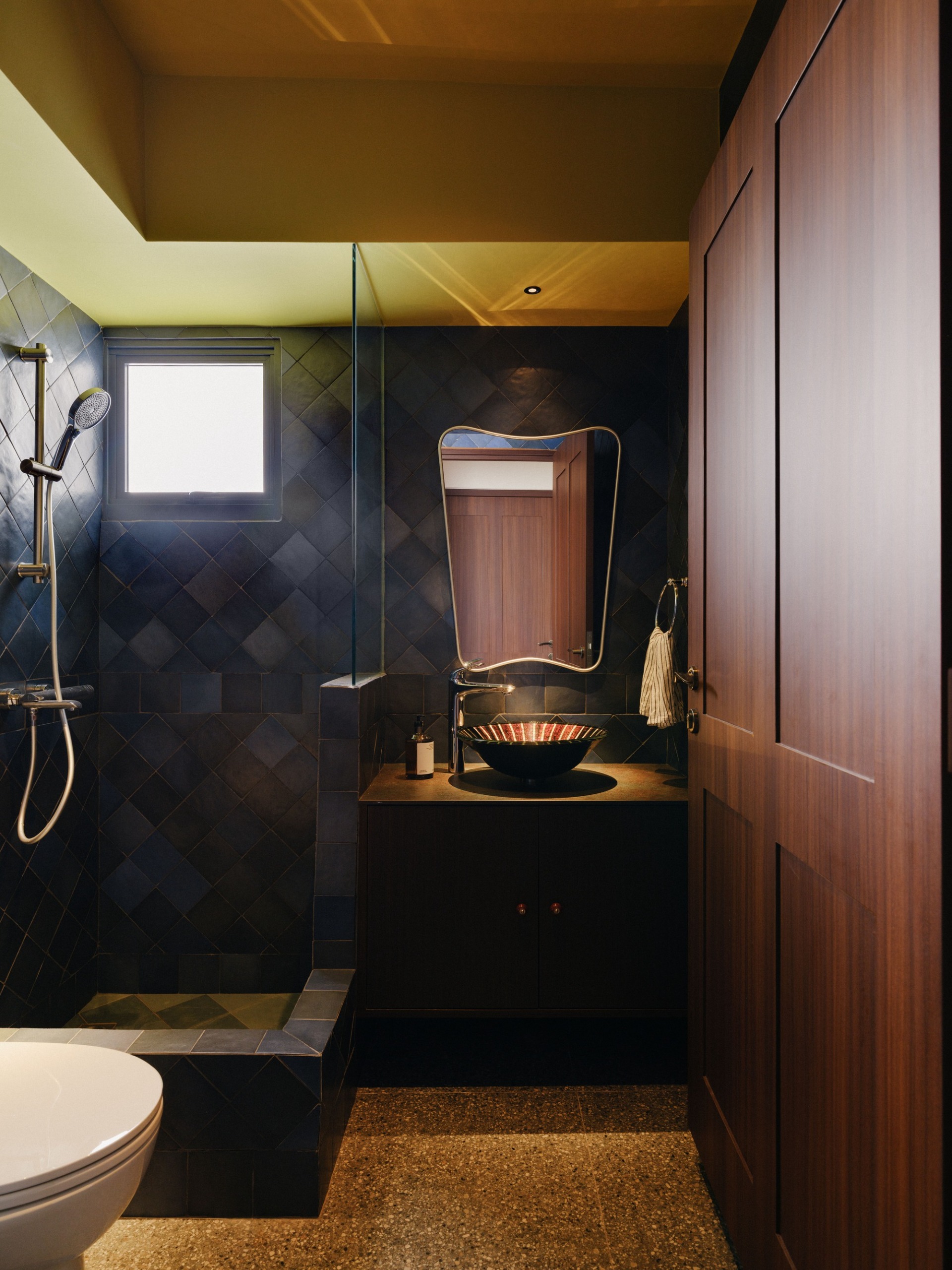 a moody bathroom with dark blue tiles, a mirrored vanity and terrazo speckled flooring