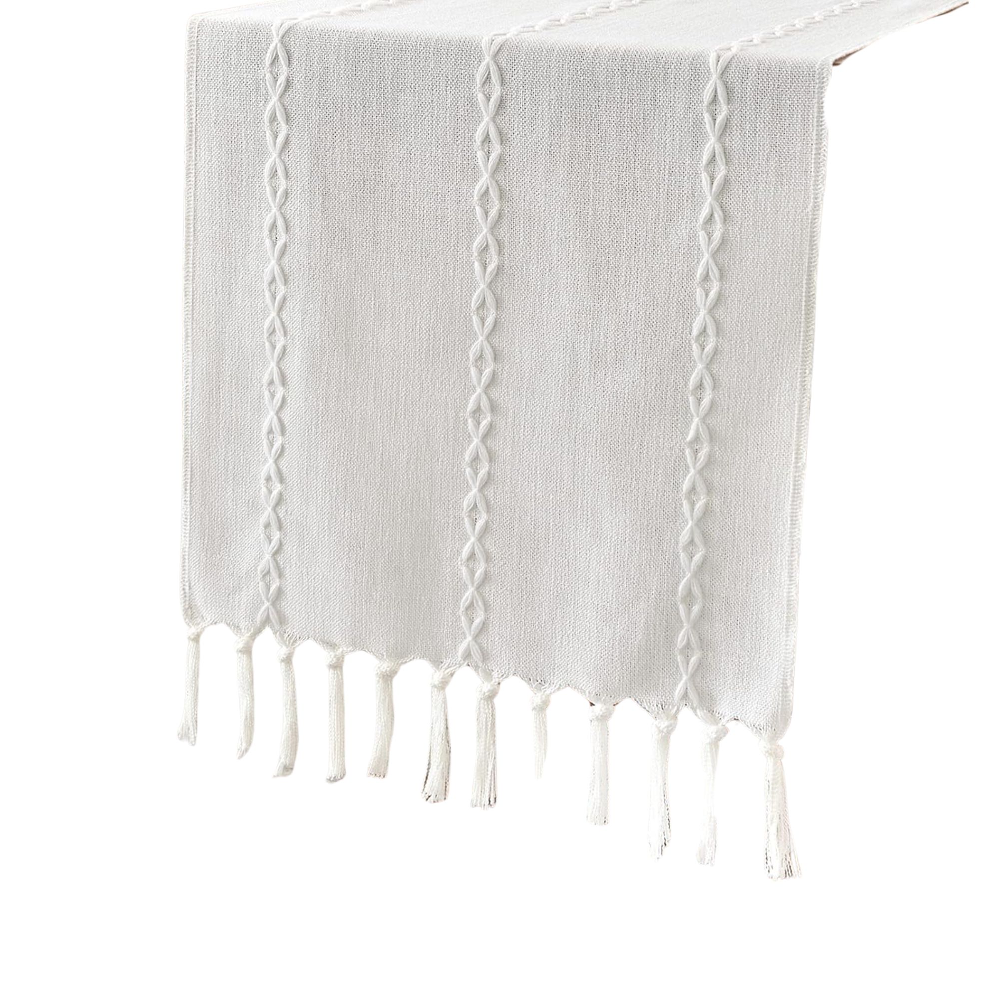 A white table runner with tassels and an embroidered pattern on it