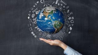 The Earth floats above an open hand in front of a blackboard with chalk drawings