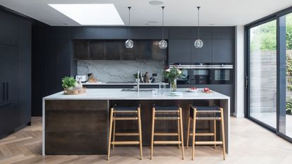 Large kitchen island clad in wooden batons with tall black units behind