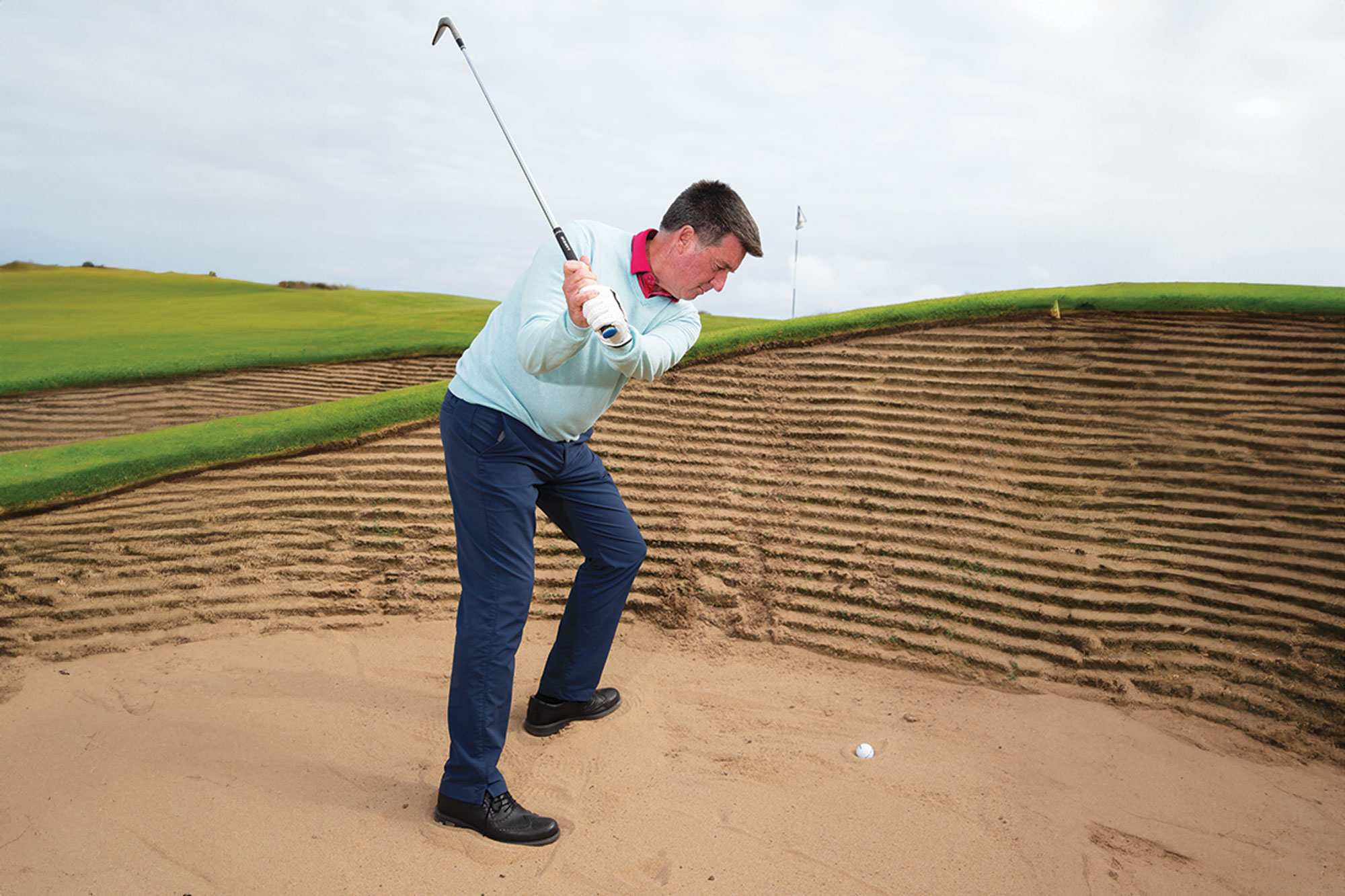 PGA Pro Clive Tucker demonstrating how to play a bunker shot from a plugged lie near the face of the bunker, at the top of his backswing
