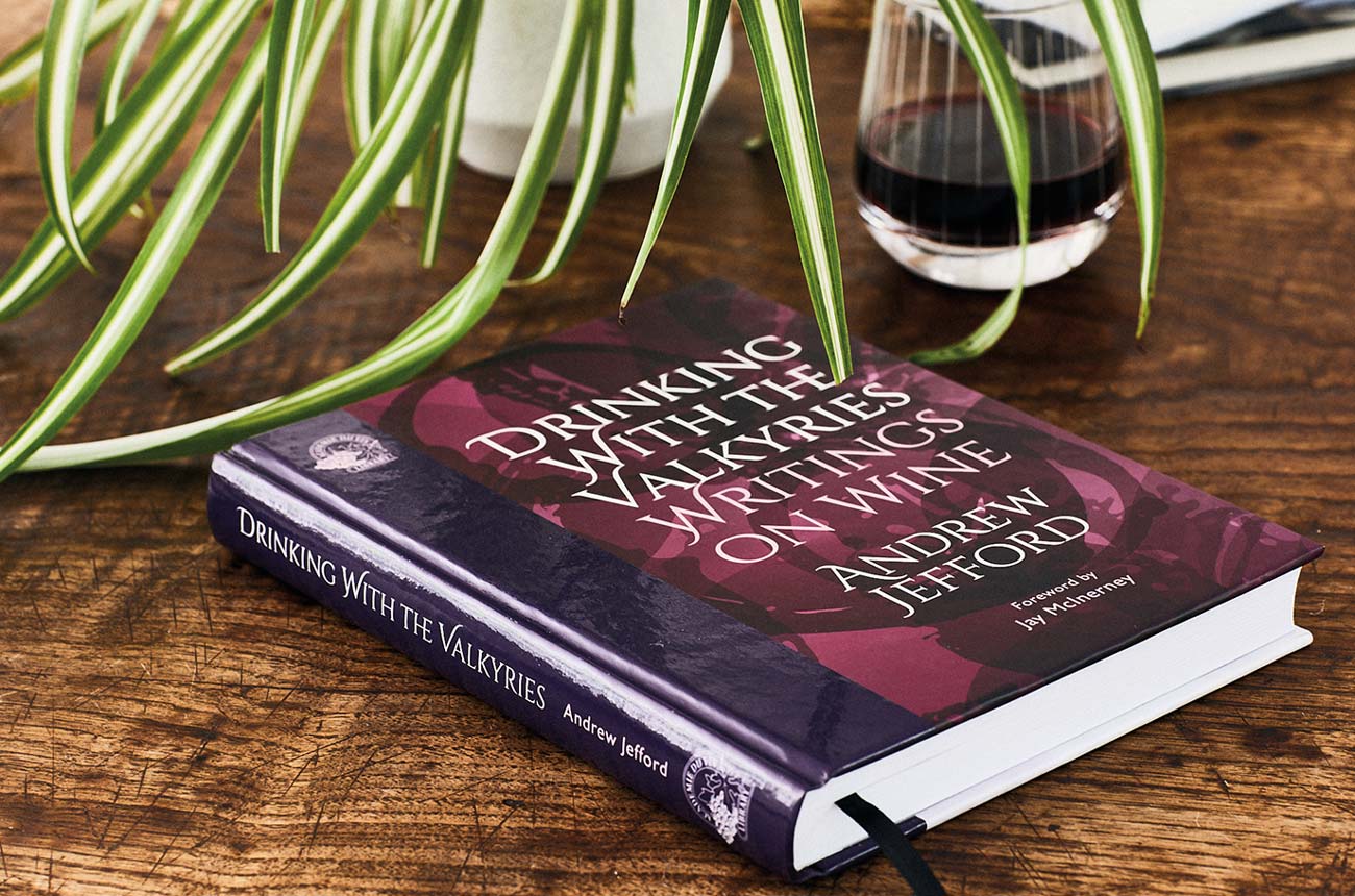 Andrew Jefford's book, Drinking with the Valkyries, on a table with a glass of wine and a plant