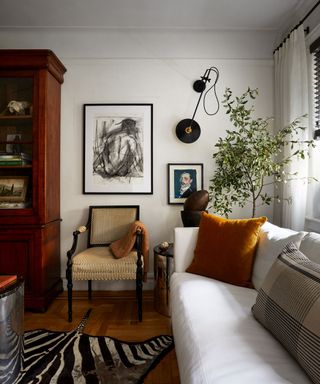 living room with white walls, white sofa and dark wood dresser, orange pillows and artwork on the walls