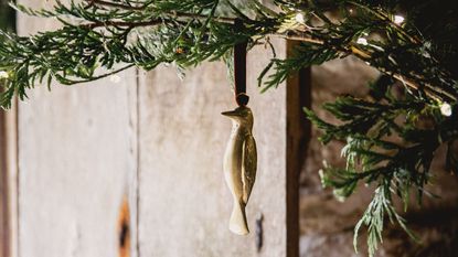 A gold bird Christmas decoration tired with a ribbon hamging from a natural christmas tree