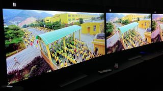 LG G3 and G2 OLED TVs in dark room with screen showing factory workers in yellow uniforms