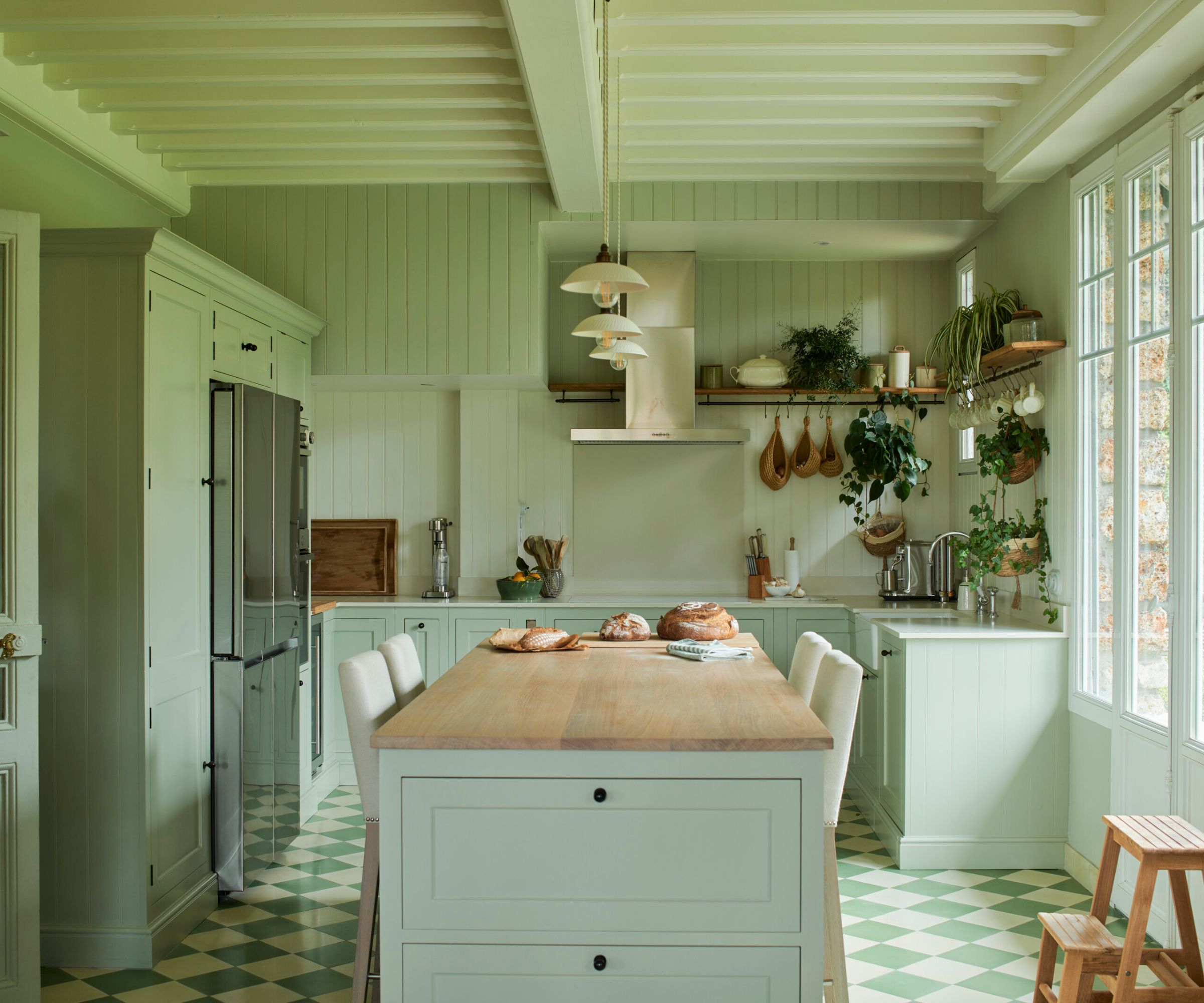 A pale blue color drenched kitchen with a wooden island countertop and a stainless steel range hood