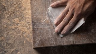 Hand with sandpaper rubbing down plank of wood