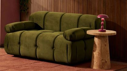 A green two-seater sofa from DUSK in a living room beside a burl wood side table and a red lamp