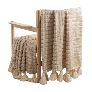 A tasseled cotton throw draped on a wooden chair
