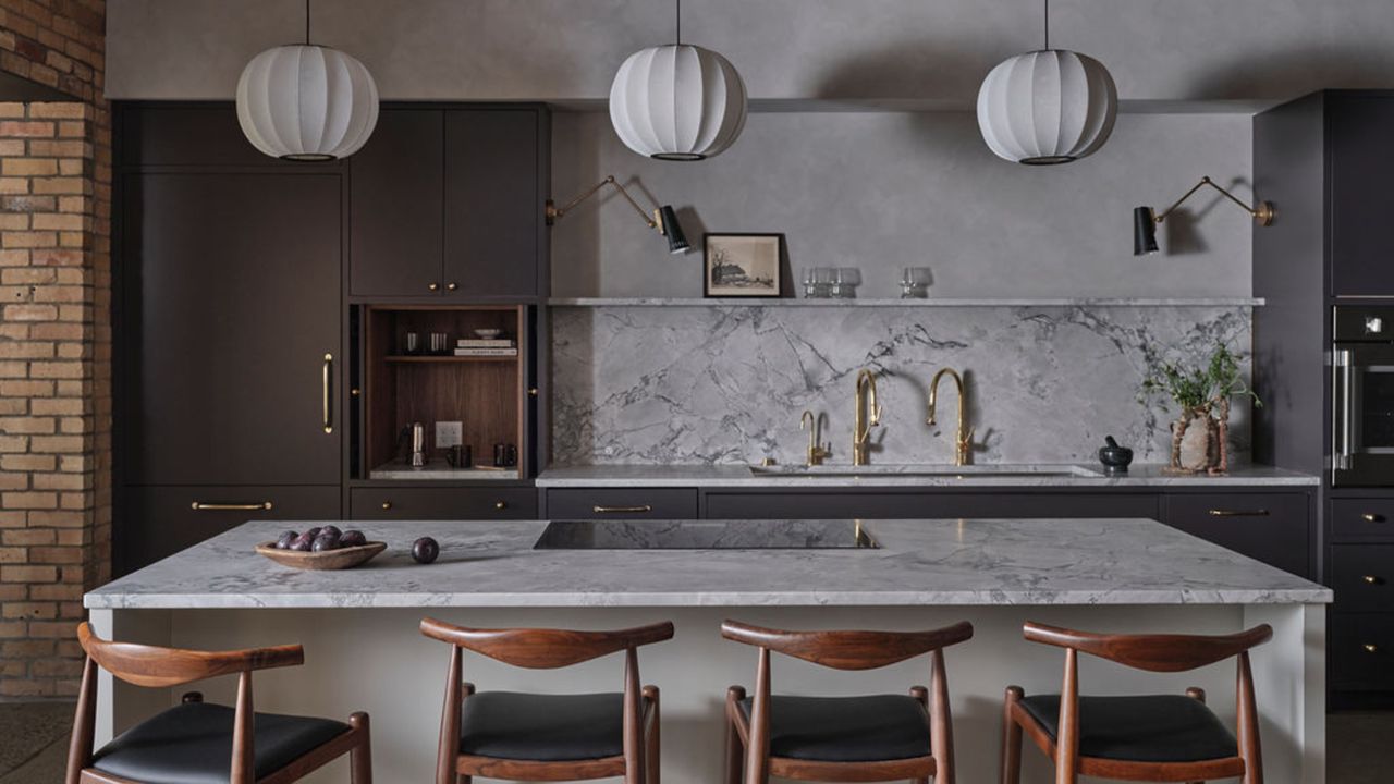 Three silk pendant lantern lights hanging over a white marble kitchen island there is dark gray cabinetry and four wooden bar stools