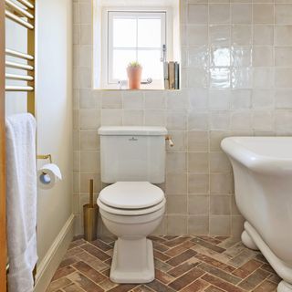 bathroom with a traditional WC and bath tub, brushed brass heated towel rail, terracotta floor tiles and a small window