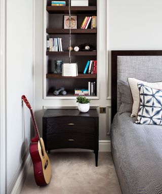 A gray bed and black chest of drawers in a small box bedroom.