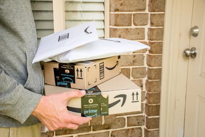 A man carrying a stack of amazon packages into a house.