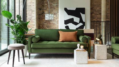 A green velvet sofa in a modern open-plan living room with exposed brick walls