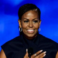 michelle obama puts her hand on her heart as she stands at a podium wearing a navy dress