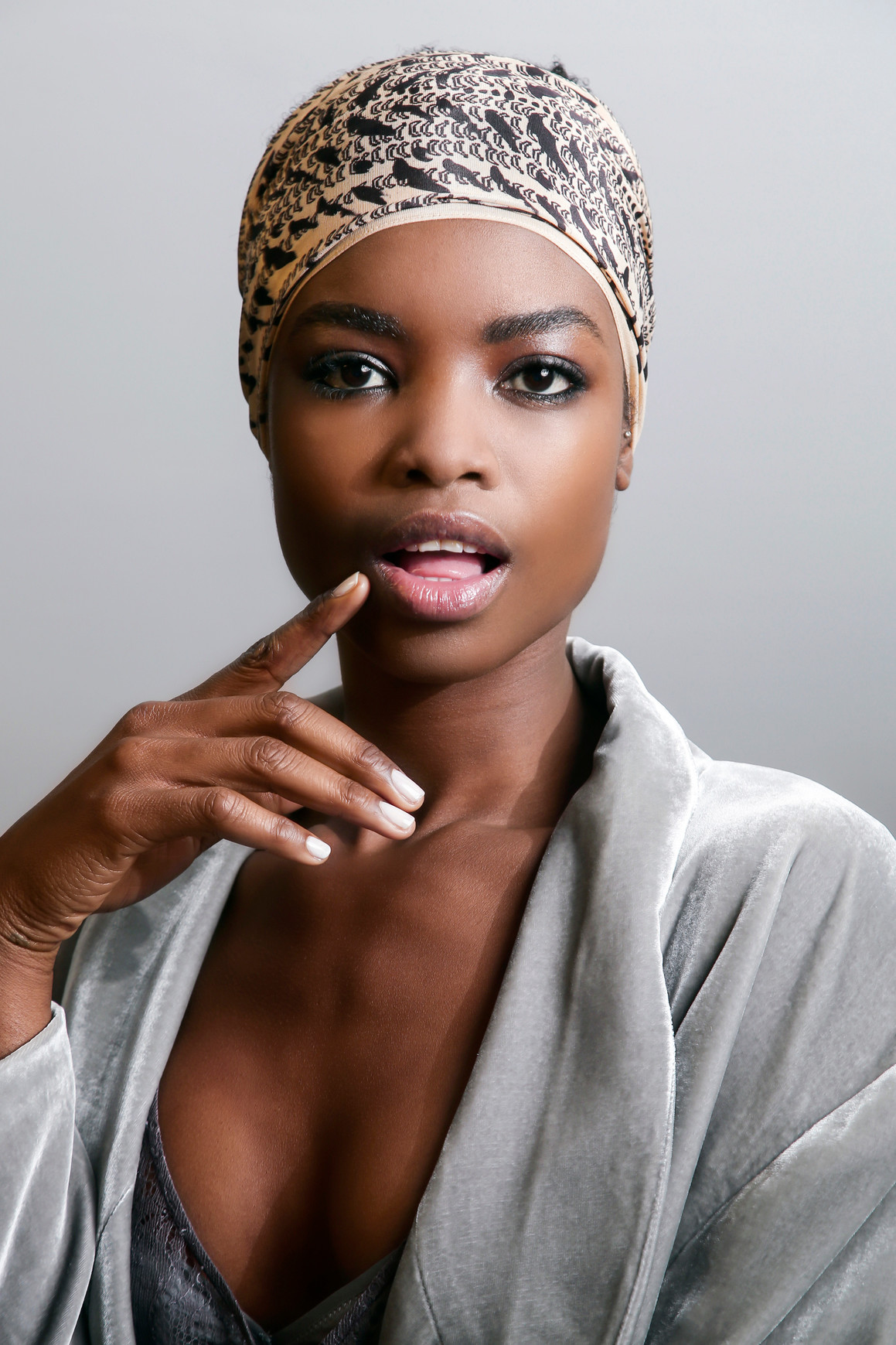 A model with milky white nails with her finger resting against her lips looking at the camera