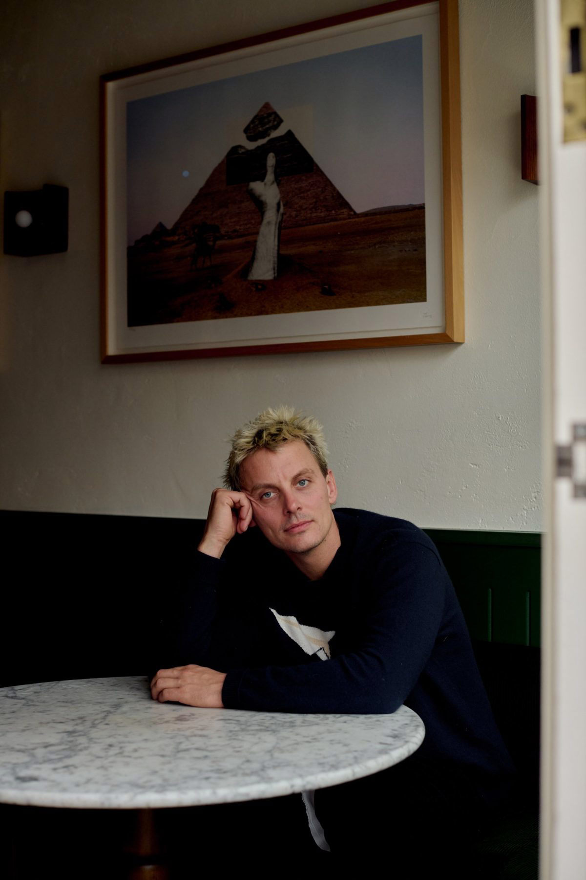 Thomas Straker sitting at a round, marble table with his head resting against one fist
