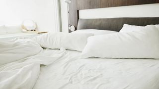 Image shows an unmade bed dressed with white linens
