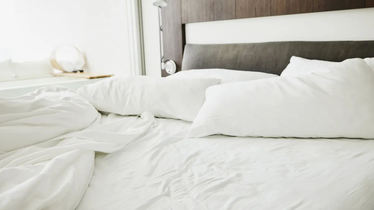 Das Bild zeigt ein ungemachtes Bett mit weißer Bettwäsche