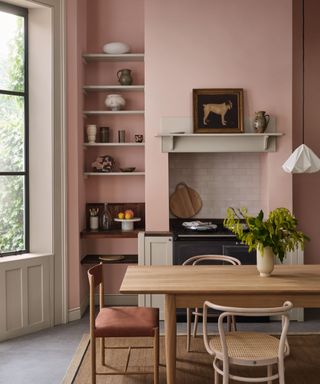 kitchen with pink walls, neutral decor and wooden dining table with vase of foliage