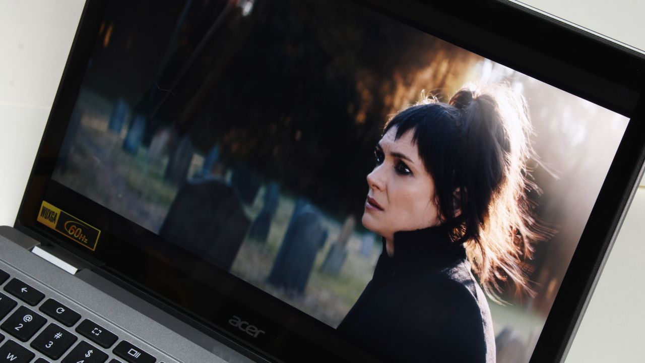 A close up of a laptop screen showing a woman with black hair sitting in a cemetery