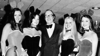 A black and white image of Eric Morecambe (centre) pictured with four Playboy Bunny Girls, including Eve Stratford (second from right) c. 1974.