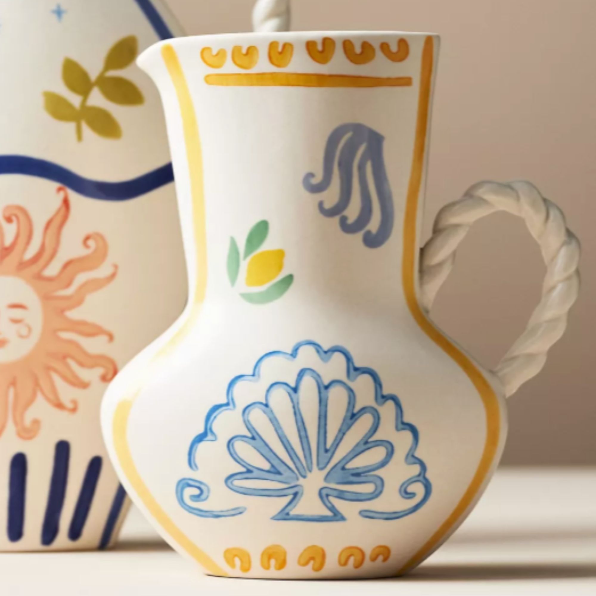 white vase with blue and yellow painted pattern and braided handle