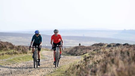 Two female riders traversing open rolling terrain along a rough gravel track. 