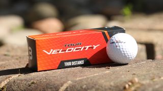 Wilson Velocity Distance Golf Ball and its firey orange packaging resting on the golf course