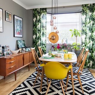 A decorative dining room with grey walls geometric rug yellow chairs and botanical print curtains