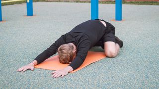 Man on yoga mat performing hip stretch outdoors in the park with arms stretched