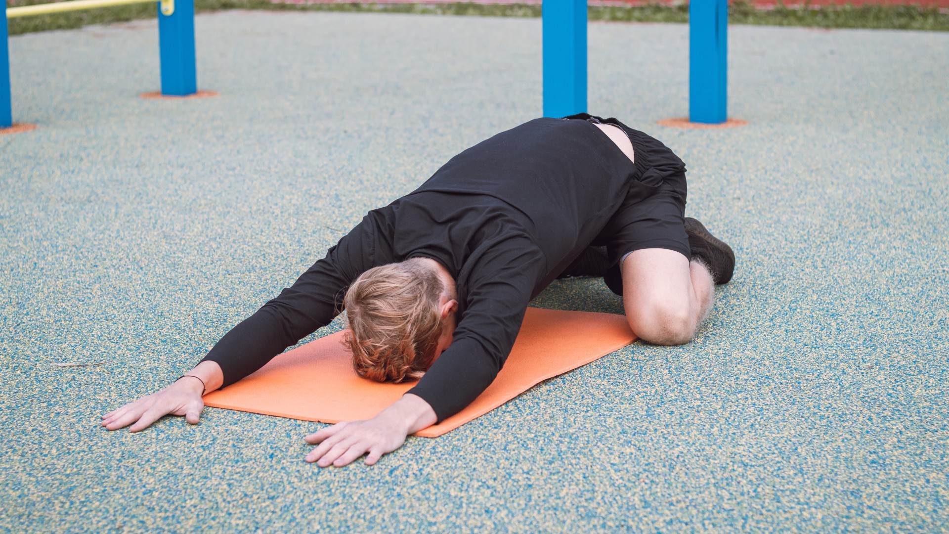 Man on yoga mat performing hip stretch outdoors in the park with arms stretched 