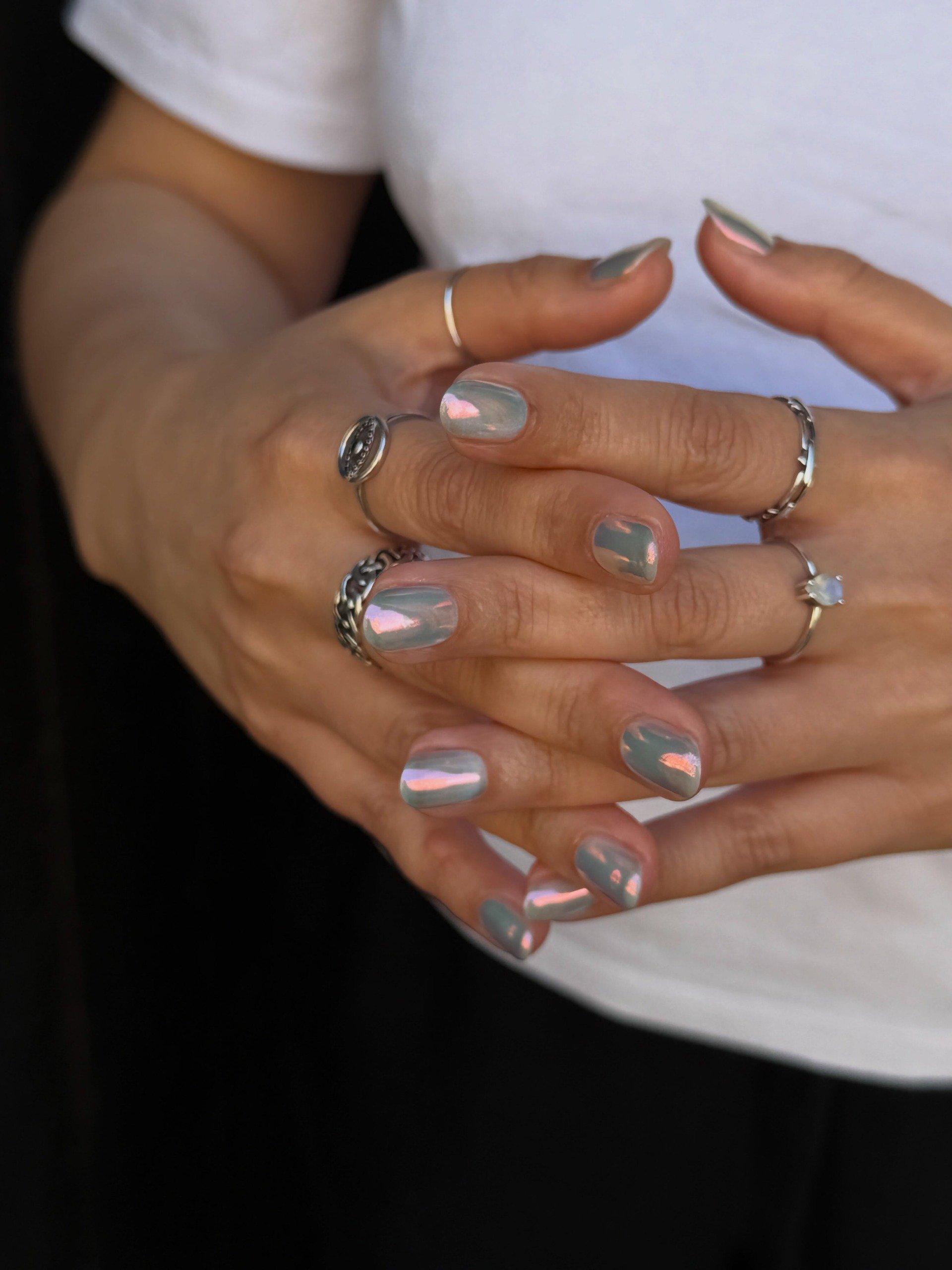 Short rounded nails coated in reflective gray chrome polish with pink pearlescent finishes