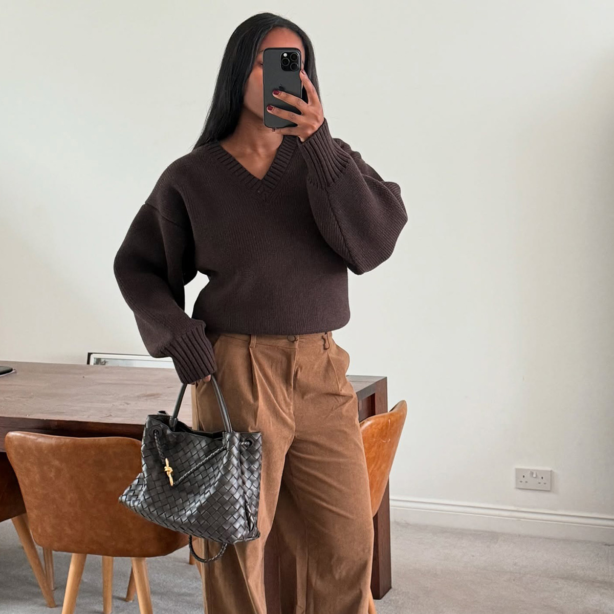 Marilyn wears a brown v-neck sweater, corduroy pants, and a black bottega veneta bag.