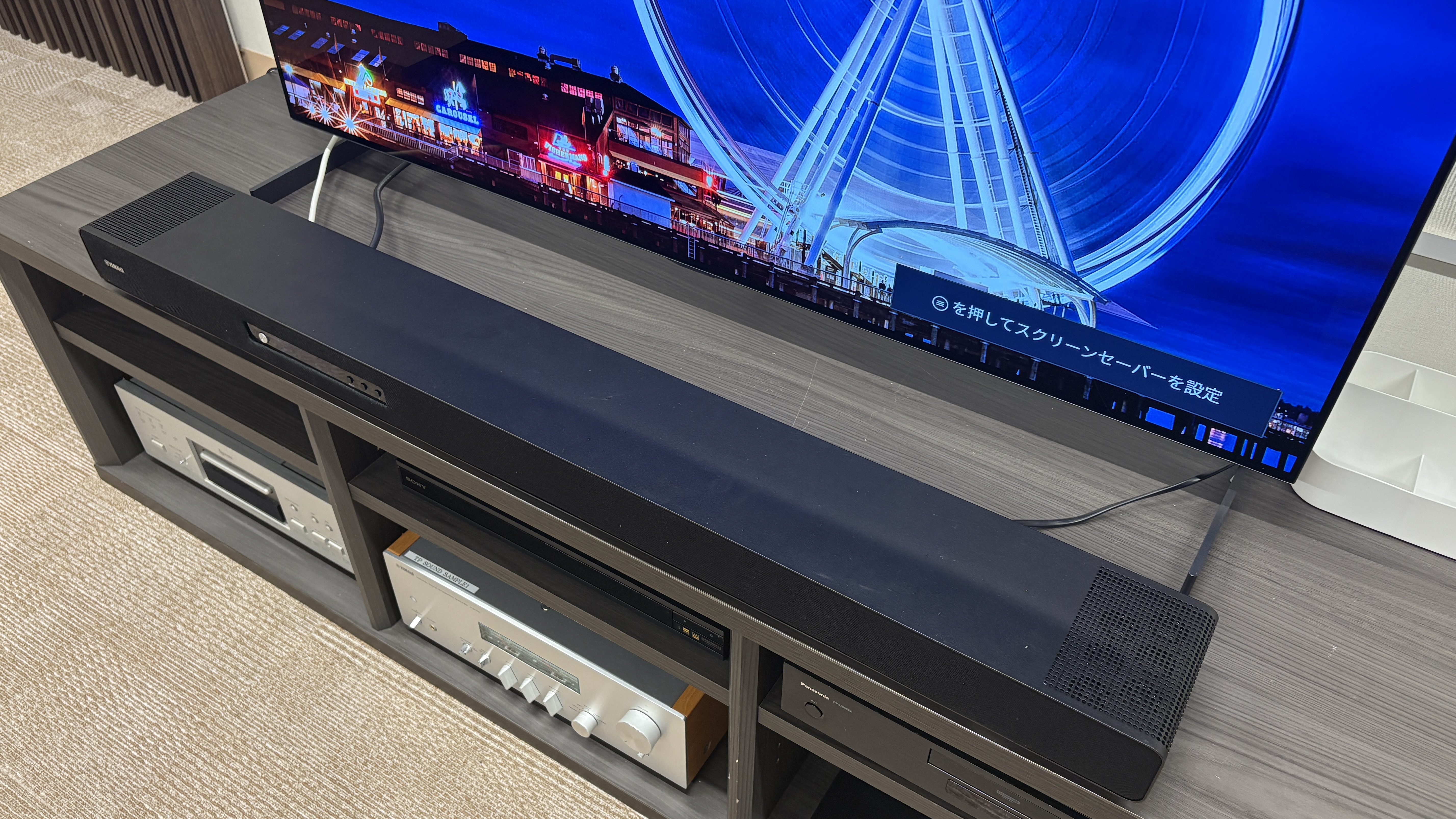 Yamaha True X Surround 90A system (soundbar, surround speakers and subwoofer) in a plain testing room with a TV.