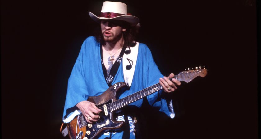 Steve Ray Vaughan wears a blue gown and a white hat as he performs with his number one Strat in 1985