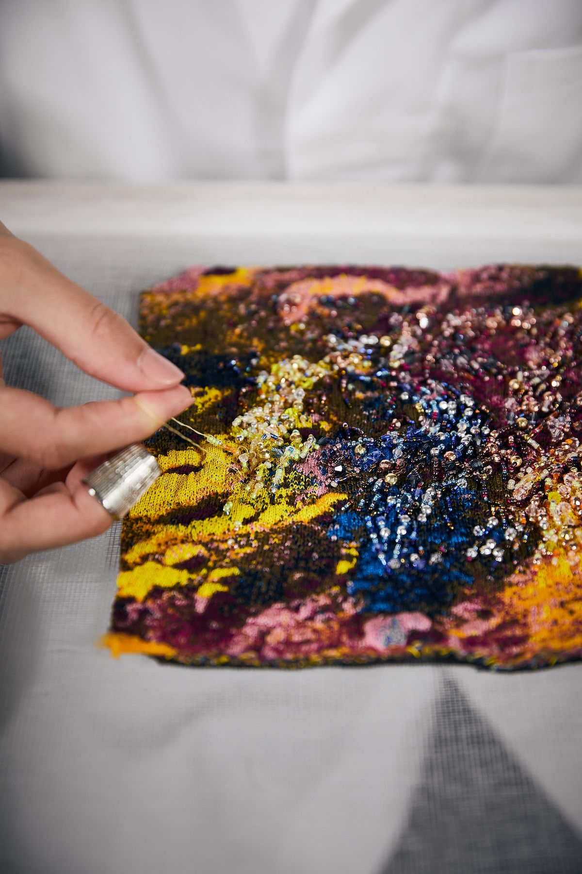 Person embroidering a colourful pattern on a handbag
