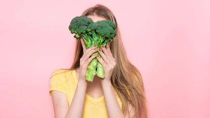 A woman holds a bunch of broccoli in front of her face.