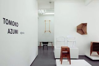 Multiple furniture items on display in a gallery . On the left of the image is the text 'Tomoko Azumi objective' written in black on a white wall