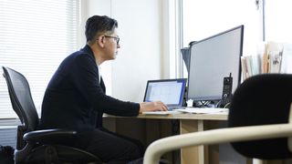 Can you use a laptop as a monitor? image shows man sitting at a desk using a PC and laptop