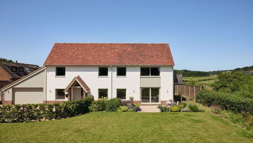 A white rendered detached house with a clay tiled roof and a green timber lean-to garage to the side