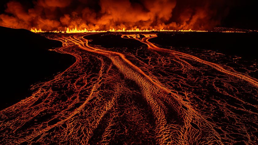 Lava flows create bright, fiery patterns against a dark landscape, illuminated by flames and smoke rising into the night sky
