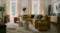 a large living room with neutral walls, large mustard yellow sectional at the center, eclectic art and objects, a neutral textured rug with a small dog lying on it