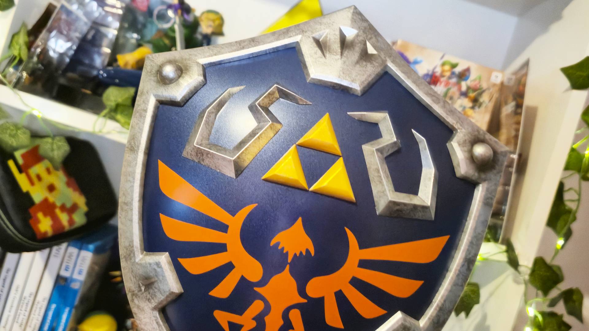 Photo of the F4F Hylian Shield sitting in front of a bookcase covered with Zelda merch.