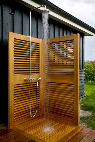 Water running from shower tap fitting in outdoor shower with wooden screens