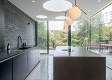 a stylish, minimalist kitchen extension by Ar'Chic - with black/grey units, a large black/grey island, slate floors and wrap around floor-to-ceiling doors/windows