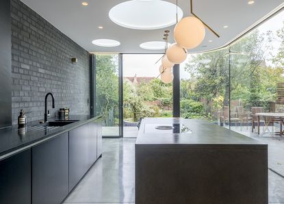 a stylish, minimalist kitchen extension by Ar'Chic - with black/grey units, a large black/grey island, slate floors and wrap around floor-to-ceiling doors/windows