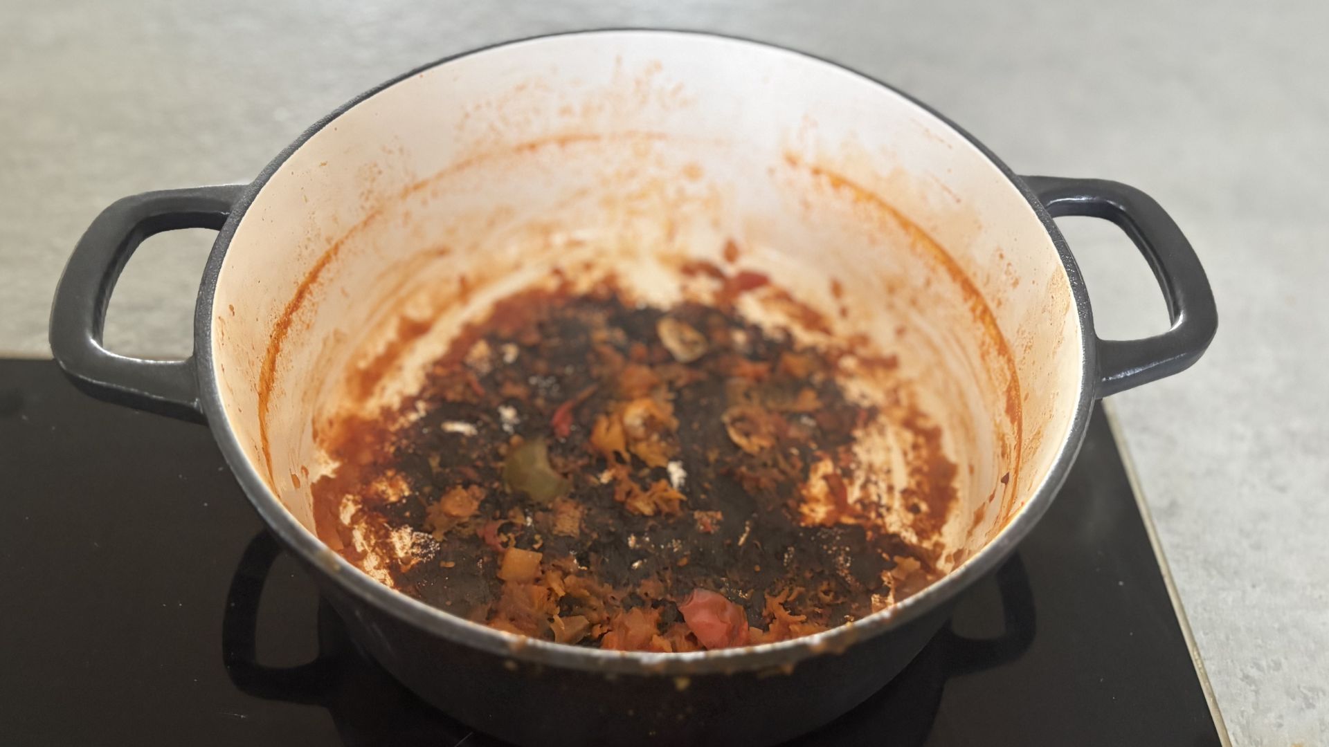 A stage of cleaning a burnt cast iron casserole dish on a hob