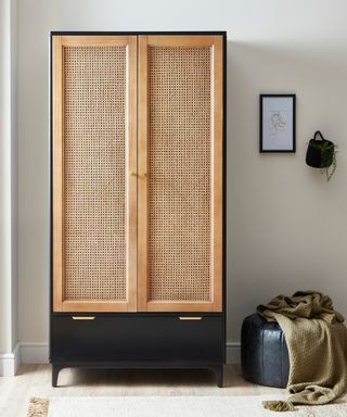 Black and rattan cane wardrobe with black leather pouffe, khaki throw, cream rug and black framed wall art